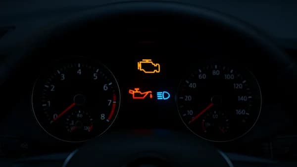 Närbild på en modern bils instrumentpanel där flera varningslampor lyser, inklusive motorlampan och oljetryckslampan.